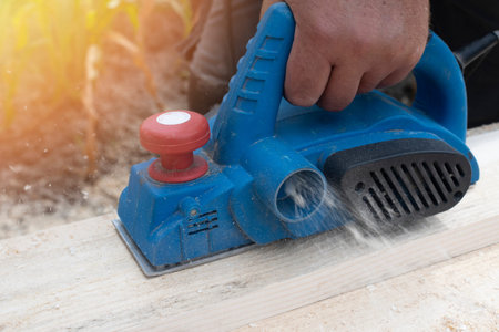 Worker's hand close-up. The process is planing boards with an electric planer.
