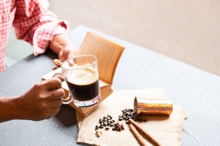 Cropped shot of man holding a cup of coffee and reading a book in the morning with ingredients. Hipster lifestyle, Travel inspiration, Cafe shop.の写真素材