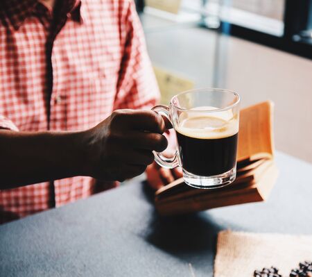 Cropped shot of man holding a cup of coffee and reading a book in the morning with ingredients. Hipster lifestyle, Travel inspiration, Cafe shop.の写真素材