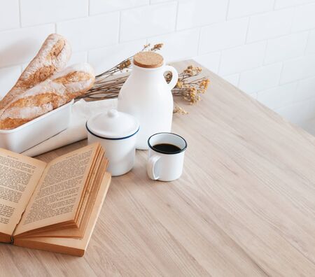 The table with a book, a cup of coffee, a jar of milk and a French bread with sunshine in morning, Beauty concept of beverage and food with relaxation and refreshment during day. Cafe shop.の写真素材
