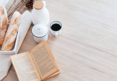 The table with a book, a cup of coffee, a jar of milk and a French bread with sunshine in morning, Beauty concept of beverage and food with relaxation and refreshment during day. Cafe shop.の写真素材