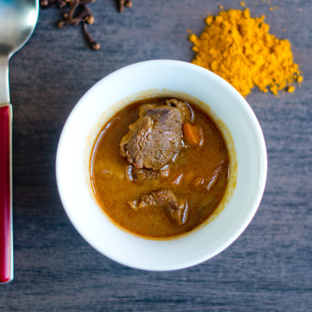 cup of tasty soup, hot and steaming with beef, vegetables, curry, turmeric and clove seeds
