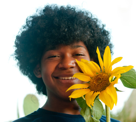 young boy smiles happily while holding a sunflower in his hand that has grownの写真素材