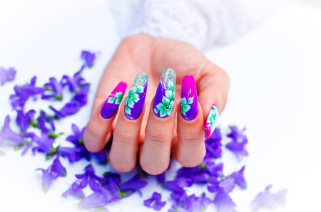 Hand with nails rebuilt and decorated with colorful flowers bring blue and white floral on white background, beautiful novelty for spring and summerの写真素材