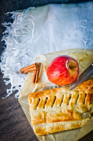 strudel homemade pie with apples and cinnamon, cut with a knife lying on cotton tablecloth decorated by hand on the kitchen tableの写真素材