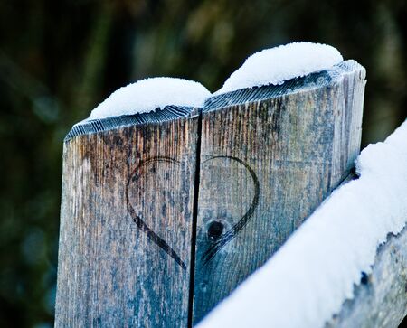 wooden fence with heart engraved for Valentine's day, in the snow that is meltingの写真素材