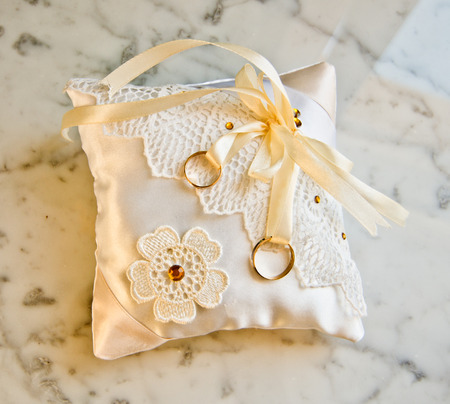 gold double rings on soft white satin pillow with handmade floral decorationsの写真素材
