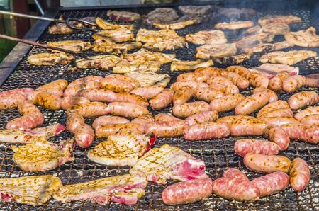 sausages and pork steaks cooked on a large barbaque with hot coals and aromatic herbsの写真素材