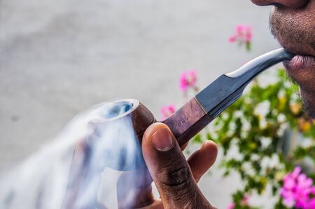 happy young man smokes with pleasure the tobacco in his pipe among sweet swirls and clouds of smokeの写真素材