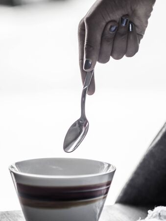 girl holds a small spoon over a mug with colorful decorationsの写真素材