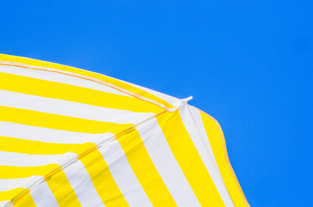 yellow and white umbrellas with the blue sky in the background, three colors symbols of summer like...