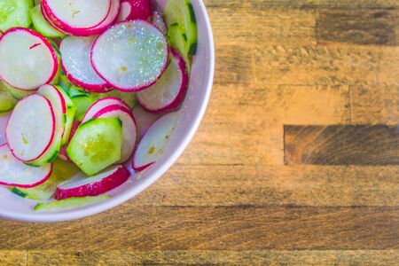 Healthy radish and zucchini salad, seasoned with vinagraitte oil, salt, pepper, vinegar and lemon juice in a bowl on a wooden board worn by time and workの写真素材