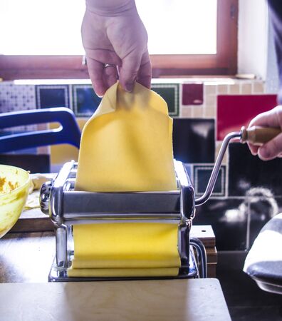 Italian housewife with traditional manual sheeter rolls egg pasta, the color of the sun of Italy, made with flour, water, egg, salt, for the party lunch.の写真素材