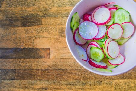 Healthy radish and zucchini salad, seasoned with vinagraitte oil, salt, pepper, vinegar and lemon juice in a bowl on a wooden board worn by time and workの写真素材