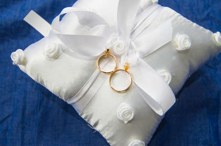 wedding rings on a white and soft pillow with beautiful and fragrant flowers, a symbol of love foreverの写真素材