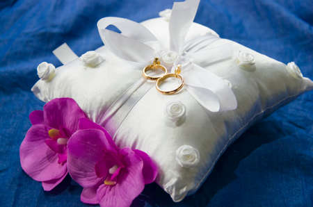 wedding rings on a white and soft pillow with beautiful and fragrant flowers, a symbol of love foreverの写真素材