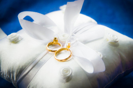 wedding rings on a white and soft pillow with beautiful and fragrant flowers, a symbol of love foreverの写真素材