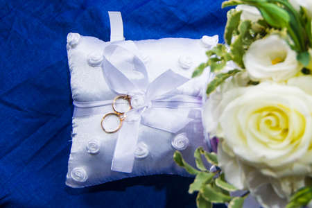 wedding rings on a white and soft pillow with beautiful and fragrant flowers, a symbol of love foreverの写真素材