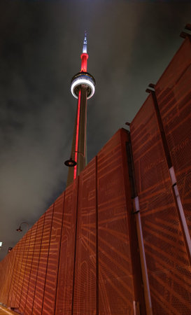 A dramatic nighttime view of Toronto's CN Tower illuminated in red light, with the bottom half of the frame covered by a red-colored iron wall or structure. The bold color and contの写真素材