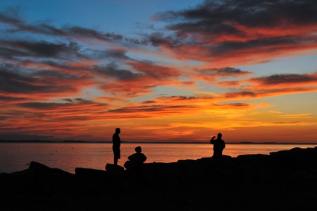 Friends silhouetted against a glorious orange sunset at Lane's Cove in Gloucester, MAの写真素材