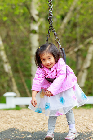 Adorable girl plays in the playground, twisted on the swingの写真素材