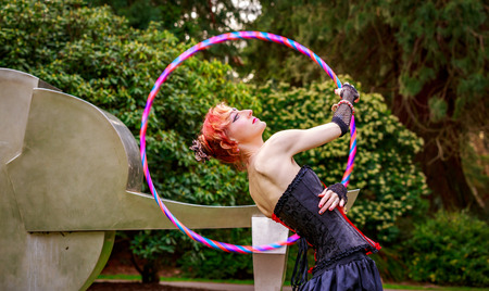 Young beautiful woman in circus costume play with hula hoop in the park.の写真素材