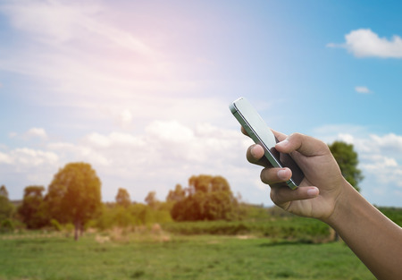 man hand hold and touch screen smart phone, tablet,cellphone on blue sky landscape in morning backgroundの写真素材