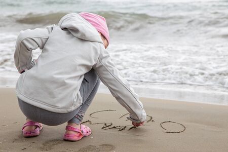CAORLE,ITALY - APRIL 2014: Young girl playing on the beach and writing in the sand.のeditorial素材