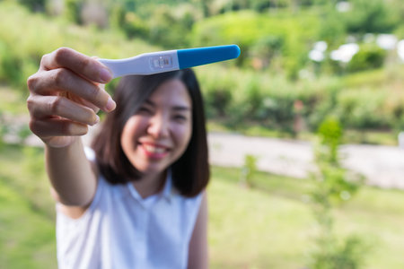 a short hair young woman smiling and showing the pregnancy test with two purple lines appeared which clearly signifies that the woman is pregnantの写真素材