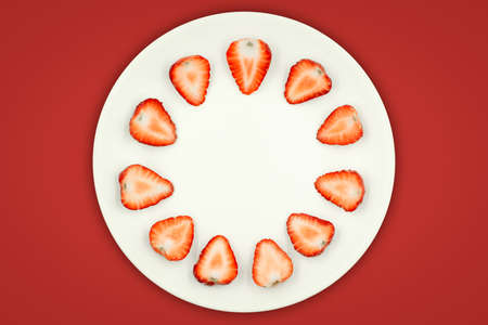Top view of half strawberry in a plate on isolated red background. Fresh strawberries are healthy fruit.の写真素材