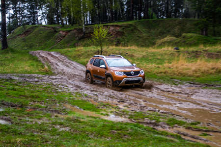 MOSCOW, RUSSIA - MAY 08, 2021 Renault Duster second generation exterior view in motion. Compact SUV car also called Dacia Duster driving across the field and dirt In the rain. Off-road obstacleのeditorial素材