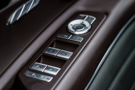 Car door handle with power window control. Dark leather interior of modern car. Dark black and orange car leather pleats stitch. Details of door handle with windows controls. car window controls.の写真素材