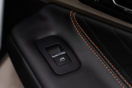 Car door handle with power window control. Dark leather interior of modern car. Dark black and orange car leather pleats stitch. Details of door handle with windows controls. car window controls.の写真素材