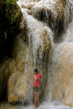 A girl standing under the waterfall, where is on the 7th level of Erawan Waterfall, Kanchanaburi, Thailandのeditorial素材