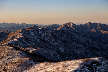 Sunrise with snow and rocks from the top of the mountain. A landscape with light and darkness along the mountain ridgeの写真素材