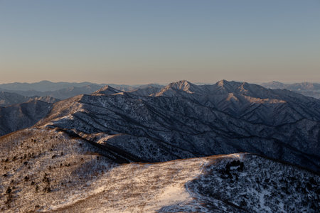 Sunrise with snow and rocks from the top of the mountain. A landscape with light and darkness along the mountain ridgeの写真素材