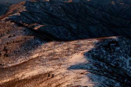 Sunrise with snow and rocks from the top of the mountain. A landscape with light and darkness along the mountain ridgeの写真素材