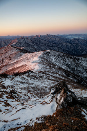 Sunrise with snow and rocks from the top of the mountain. A landscape with light and darkness along the mountain ridgeの写真素材
