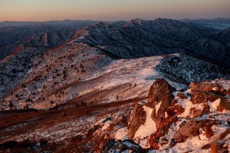 Sunrise with snow and rocks from the top of the mountain. A landscape with light and darkness along the mountain ridgeの写真素材