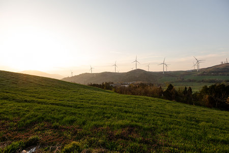 A beautiful farm with wind turbines, mountain and field sunriseの写真素材