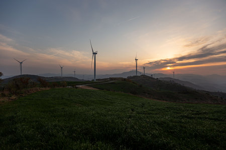 A beautiful farm with wind turbines, mountain and field sunriseの写真素材
