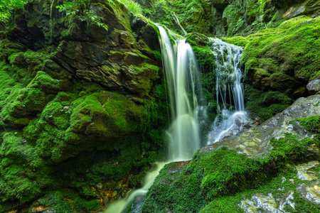 A waterfall in a deep forest full of moss on rocks, long exposure.