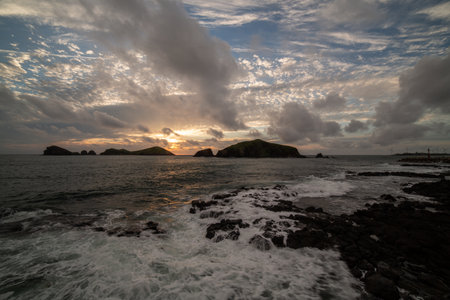 Sunset sea scenery with breaking waves and islands, colorful clouds and lightsの写真素材