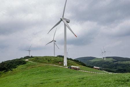 a tractor wagon that runs on a ranch with green pastures and wind turbinesの写真素材