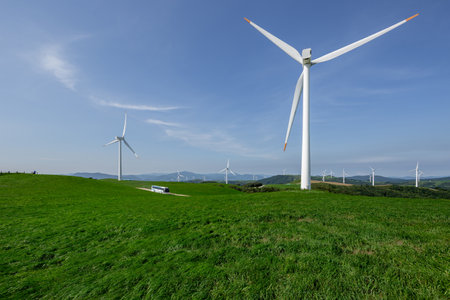 Bus running on pastures and wind farms spread out under the blue skyの写真素材