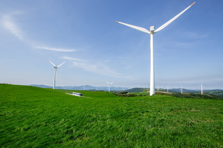 A bus running on pastures and wind farms spread out under the blue skyの写真素材