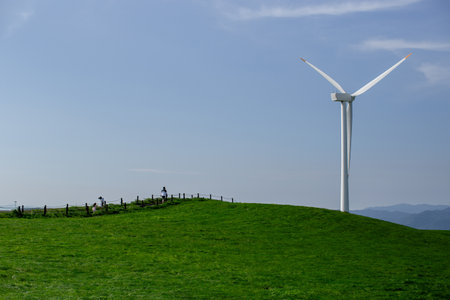 A family walking on a hill with blue skies, pastures and wind turbinesの写真素材