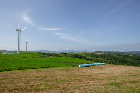 wind turbine on green meadow with blue sky and mountain in backgroundの写真素材