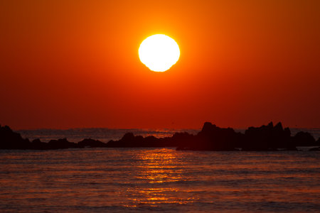 The red sun rising over the silhouette of the seashoreの写真素材