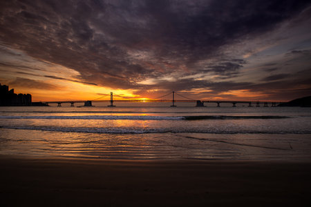 a beach sunrise with a bridge across the seaの写真素材